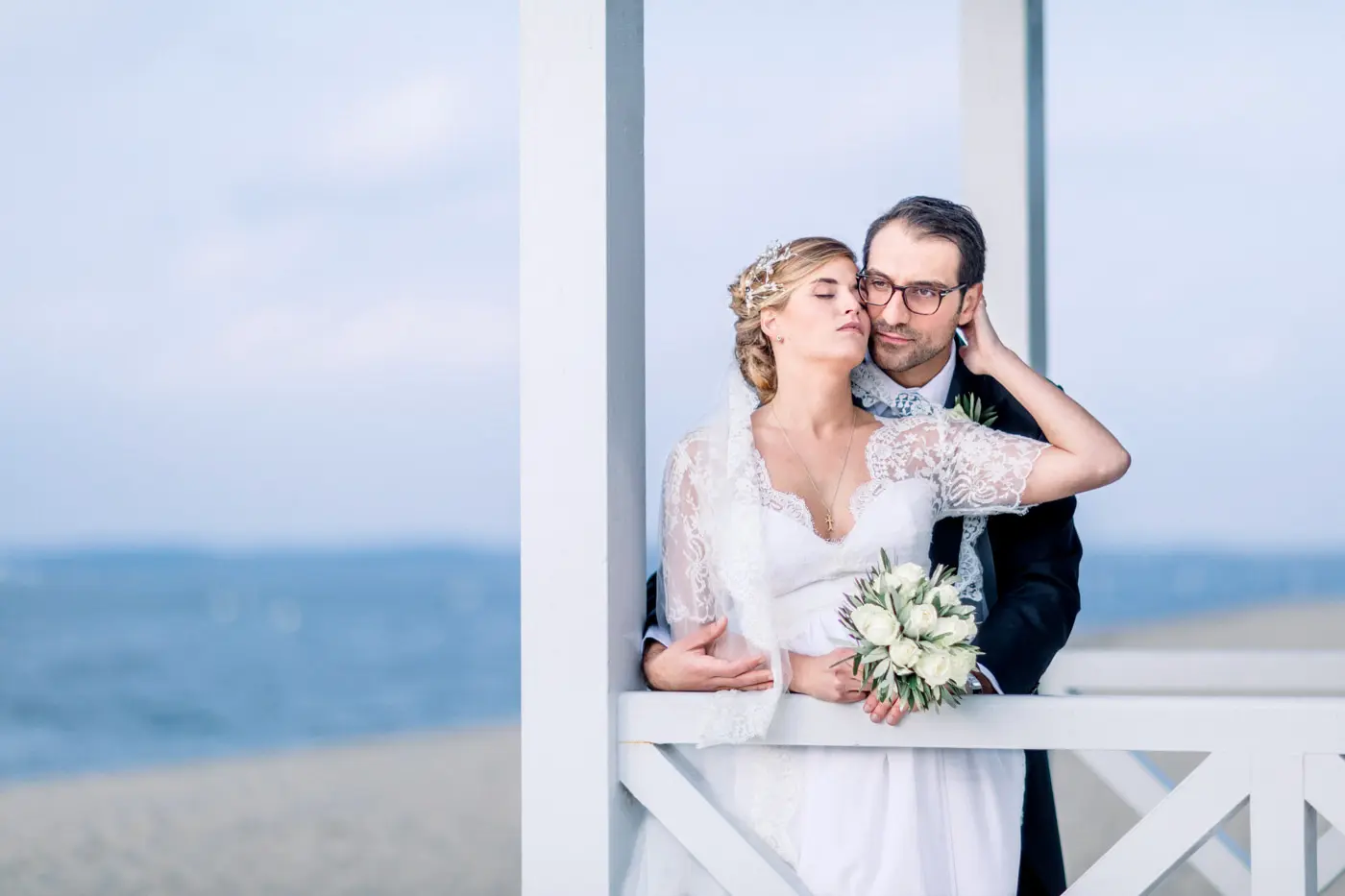 Bride and groom embracing on a white wooden veranda by the water