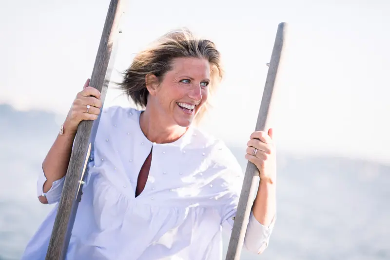 Smiling woman in a white blouse between two wooden posts by the bay