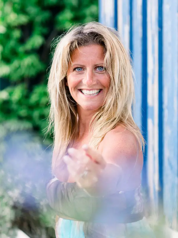 Smiling blonde woman reaching out in front of a blue hut