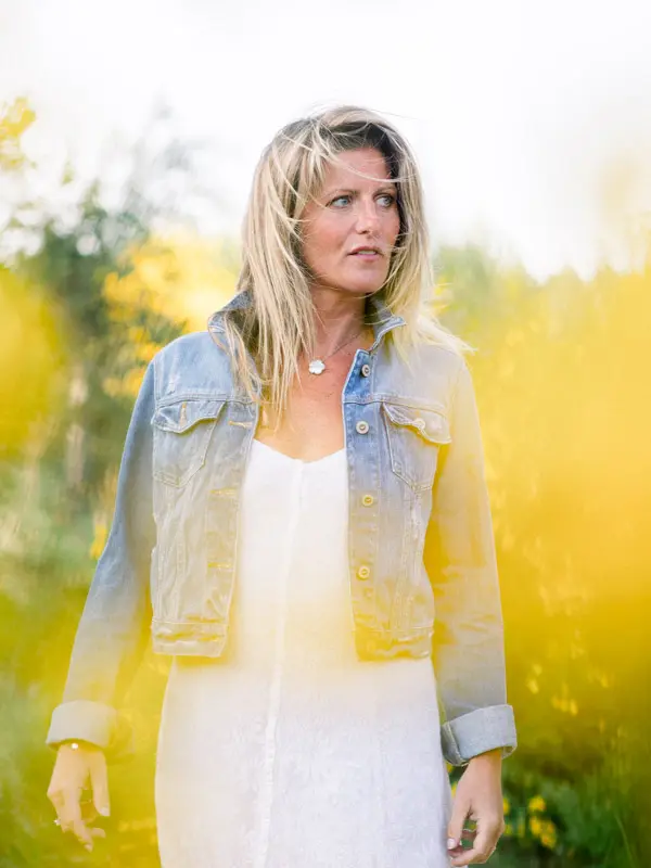 Woman in a denim jacket and white dress in front of flowering broom