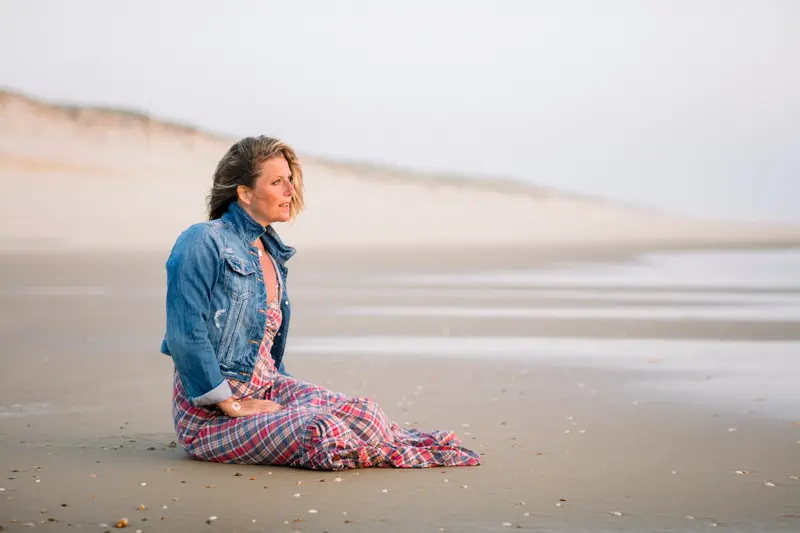 Woman sitting on the sand at the foot of the dune at dusk