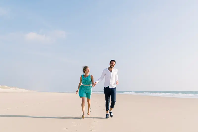 The engaged couple strolling on the sand by the ocean