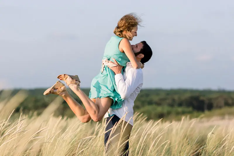 He lifts her up in her turquoise dress among the dune grasses