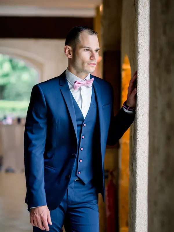 Groom in a blue suit and pink bow tie waiting in a doorway