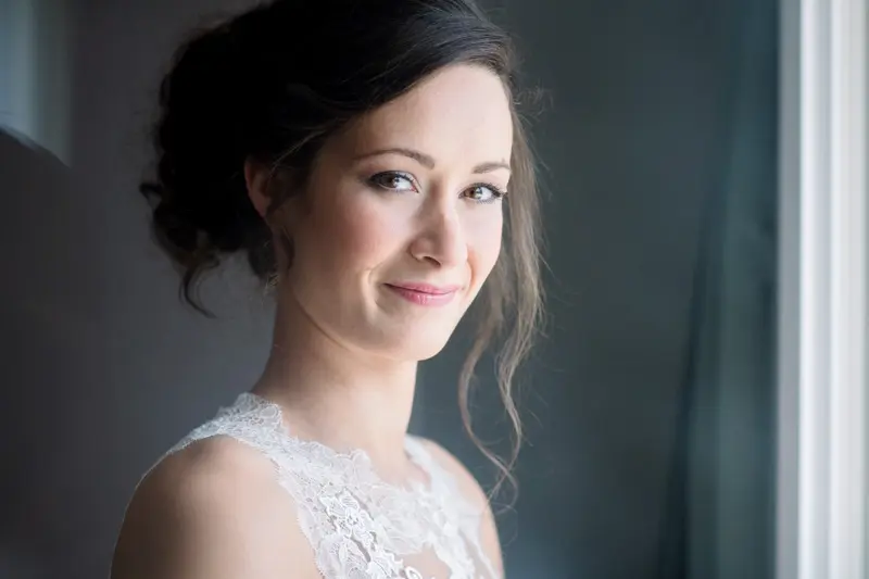 Bride smiling by a window, soft light on her face