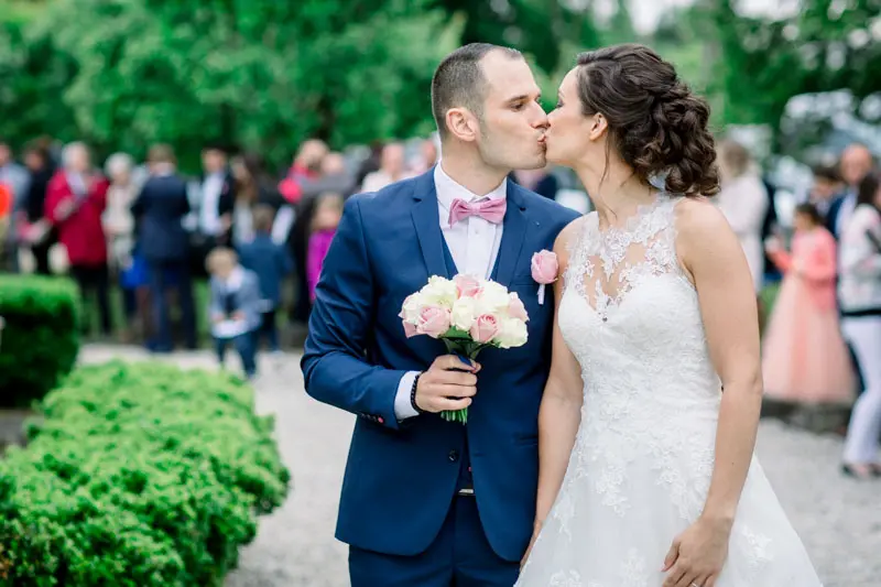 Bride and groom kissing on the manor path, guests behind them