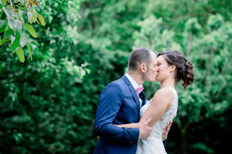 Bride and groom kissing against the greenery of the Manoir de Saint-Gervais grounds