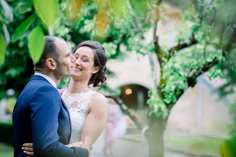 Bride and groom smiling at each other beneath a garden tree