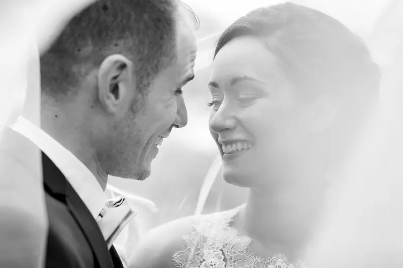 Bride and groom smiling under the veil, black and white photo
