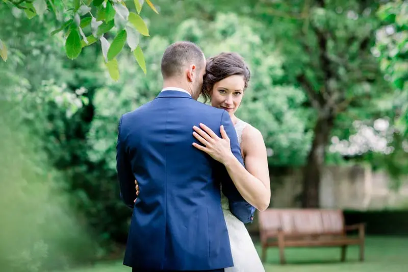 Bride and groom embracing near a bench in the manor garden