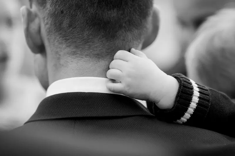Baby's hand resting on the back of a man's neck, black and white