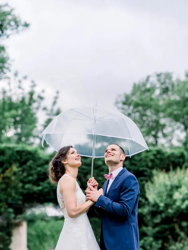 Bride and groom under a clear umbrella on a rainy day at the manor