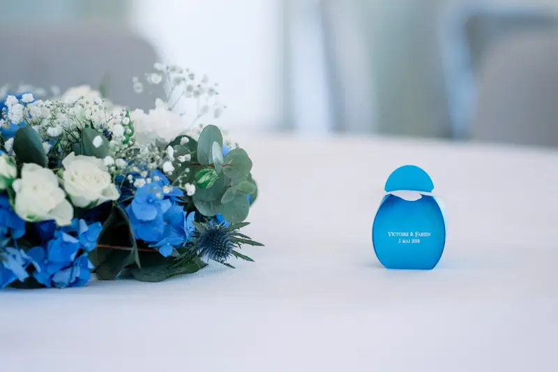 Centrepiece of blue hydrangeas and white roses beside a small blue bottle
