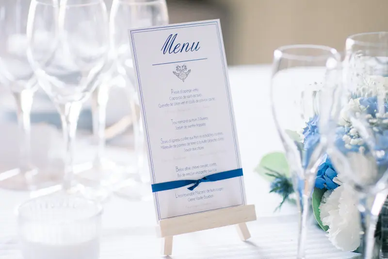 Wedding dinner menu on a small easel among the glasses, blue and white décor