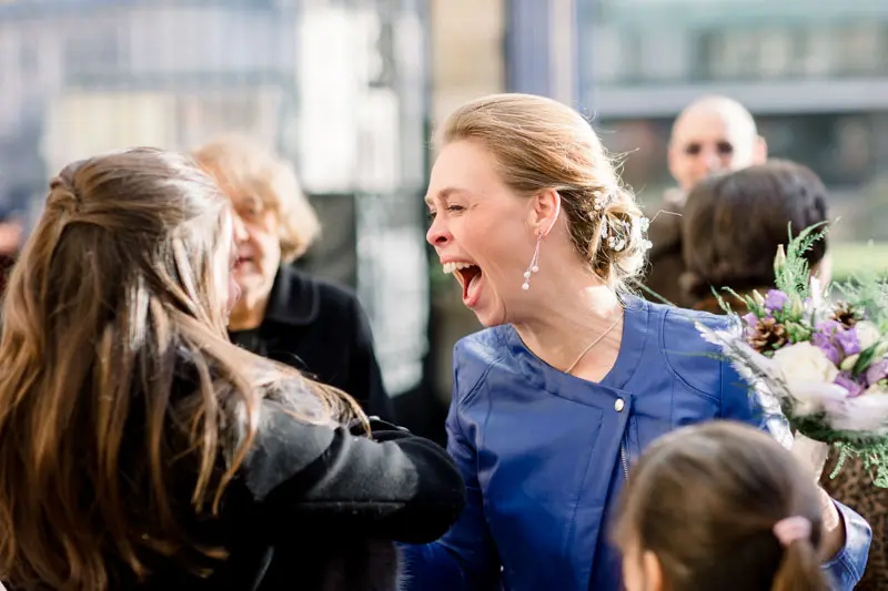 Bride in a blue jacket laughing heartily with her guests
