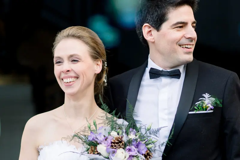 Bride and groom smiling, holding a bouquet of purple flowers