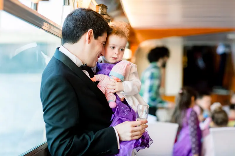 Groom holding a little girl in a purple dress aboard the boat