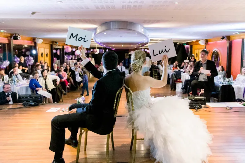 Bride and groom back to back holding up Moi and Lui signs during a game