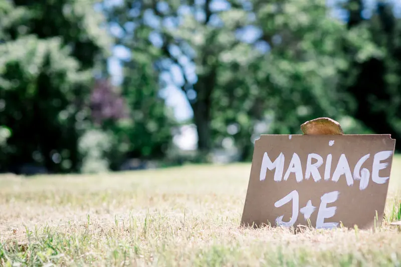 Cardboard Mariage J+E sign planted in the grass of a meadow