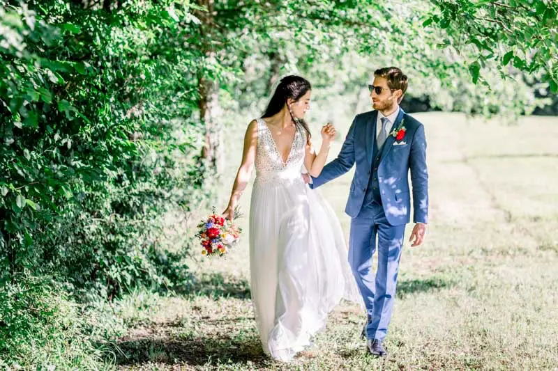 The newlyweds walking hand in hand through a tree-lined meadow