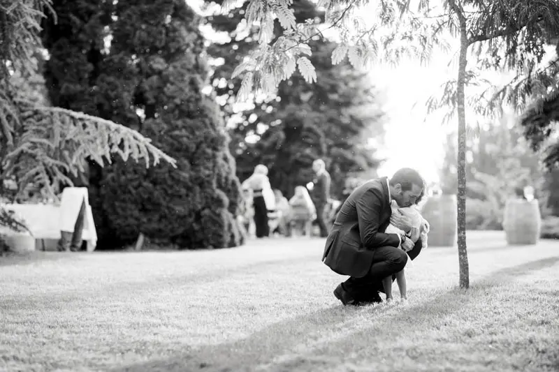 A father crouching to hug his child on the lawn, in black and white