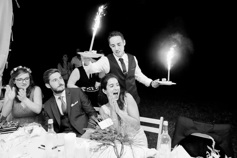 The wedding cake arriving with sparklers in front of the couple, in black and white