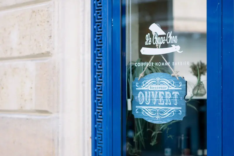 Blue shopfront of Le Coupe-Chou barbershop with an "Ouvert" sign in Chartrons
