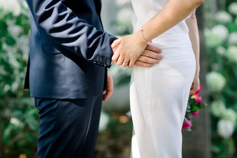 Bride and groom's hands touching against the park greenery