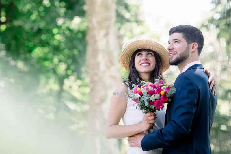 Bride in a straw hat with a colourful bouquet in the groom's arms