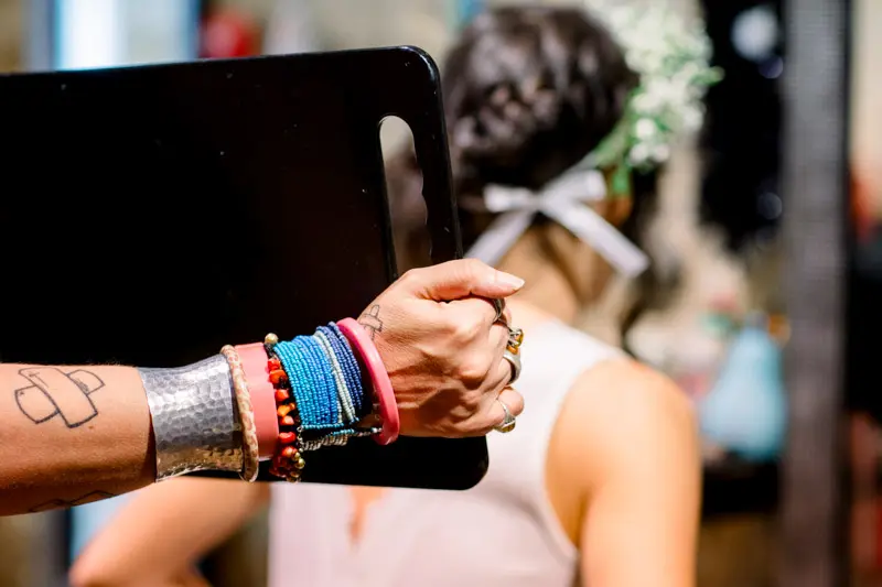 Hairdresser with bracelet-covered arm holding a mirror behind the bride