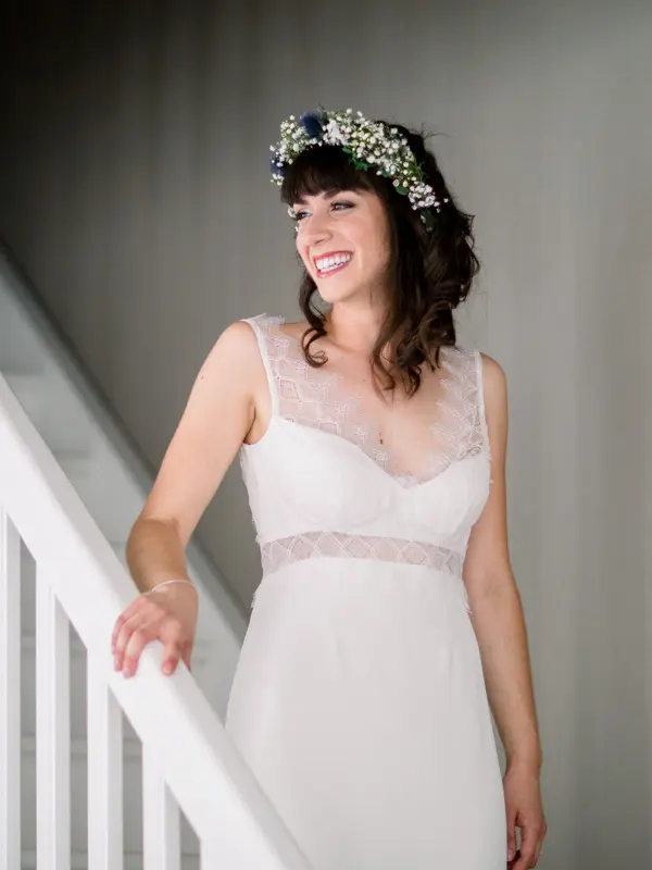 Bride in a white dress smiling on the staircase, flower crown