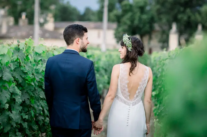Couple seen from behind holding hands in the vines, the bride's lace-back dress