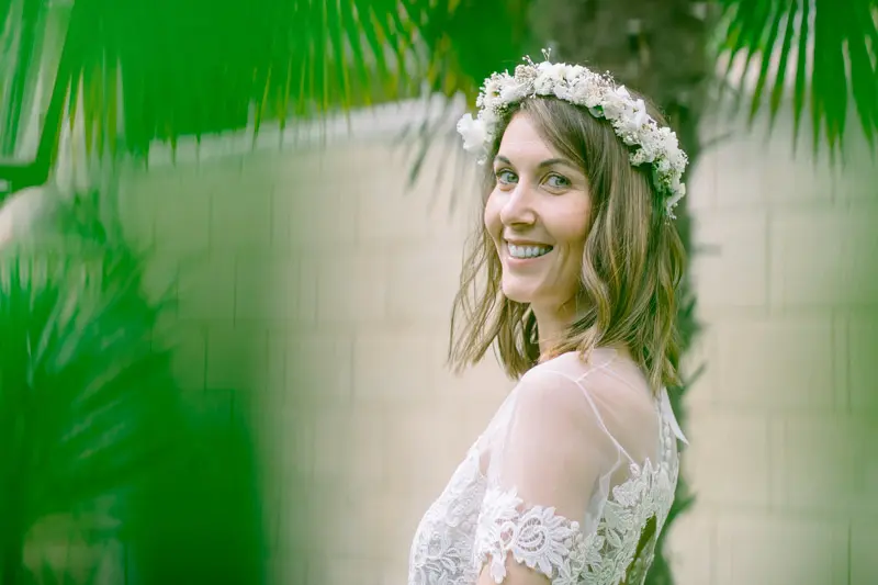 Smiling portrait of the flower-crowned bride through palm fronds