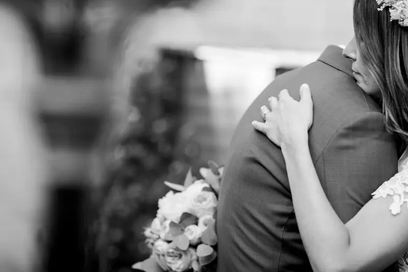 The bride hugs the groom, bouquet in hand, in black and white