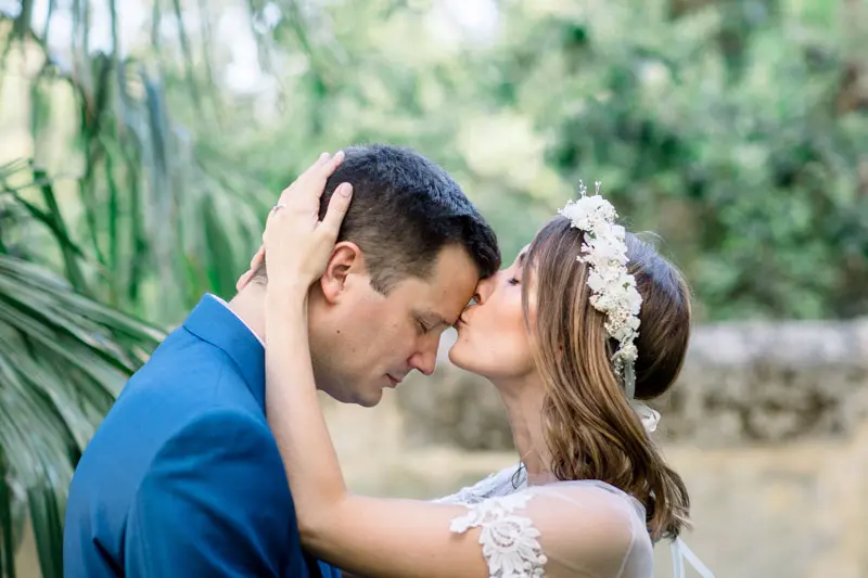The bride kisses the groom's forehead among the palm trees