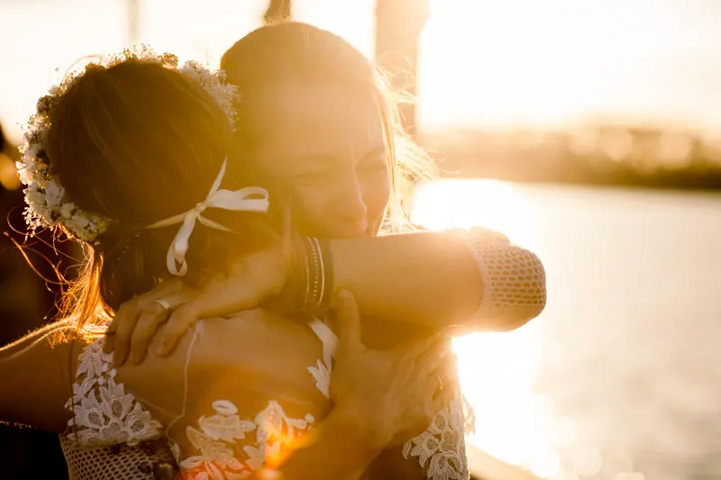 The bride sharing a warm hug with a guest, backlit by the sun