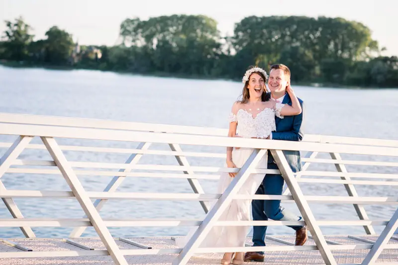 The newlyweds embracing on the white jetty by the river