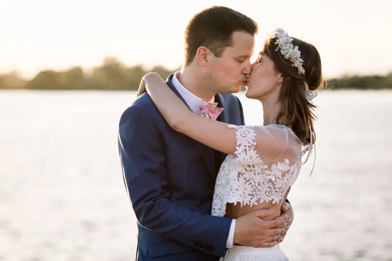 The bride and groom kiss in the setting sun facing the river