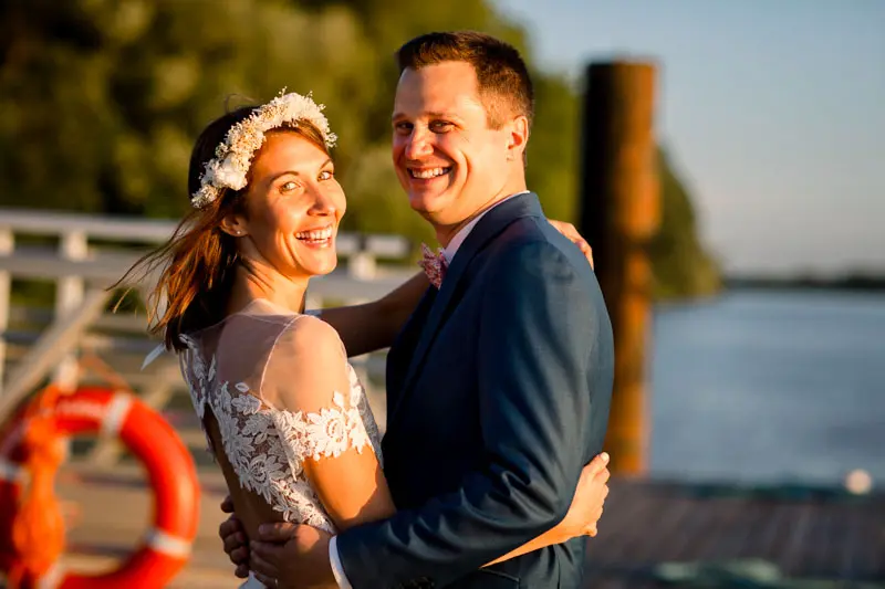 The newlyweds laughing in an embrace on the jetty beside a red lifebuoy