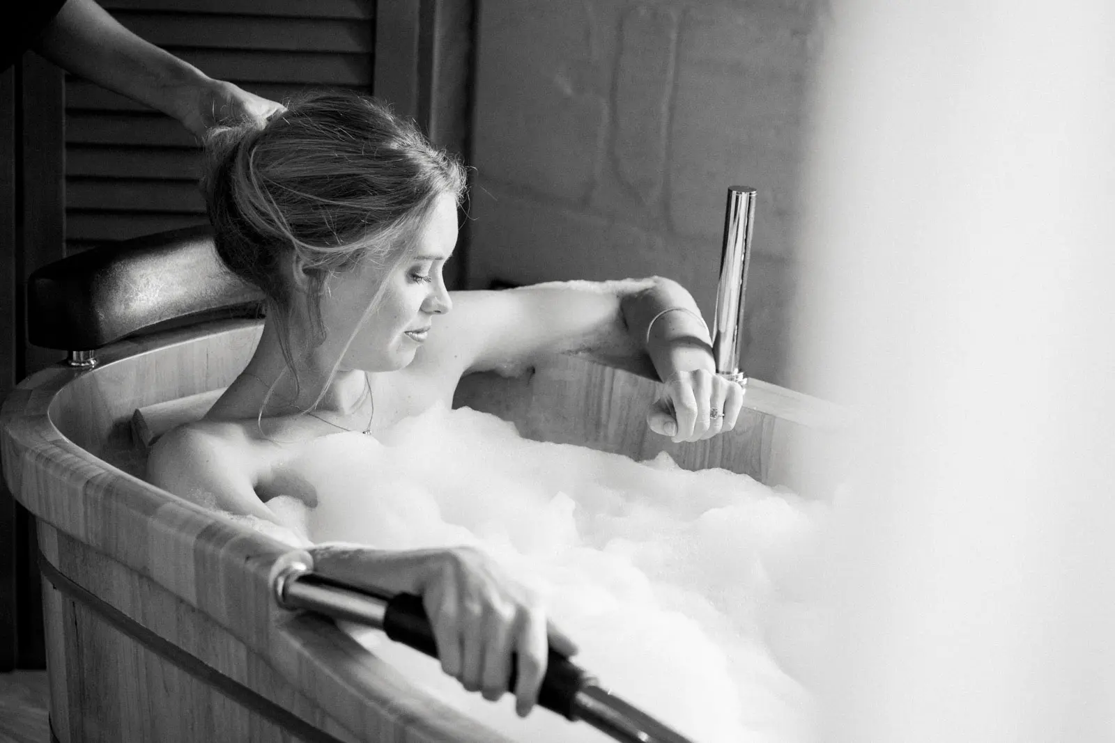 Bride relaxing in a bubble bath while getting ready, in black and white