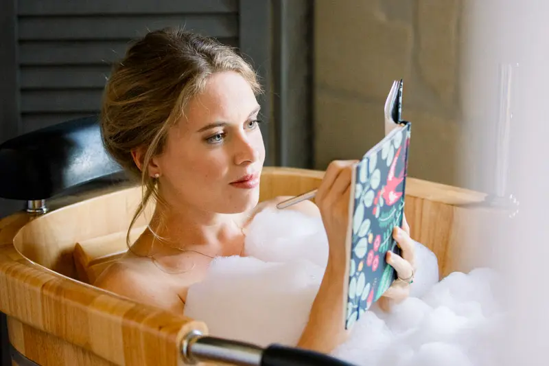 Bride reading a letter in her foam-filled wooden bathtub