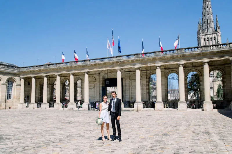 The newlyweds in the cobbled courtyard of Bordeaux town hall, flags flying