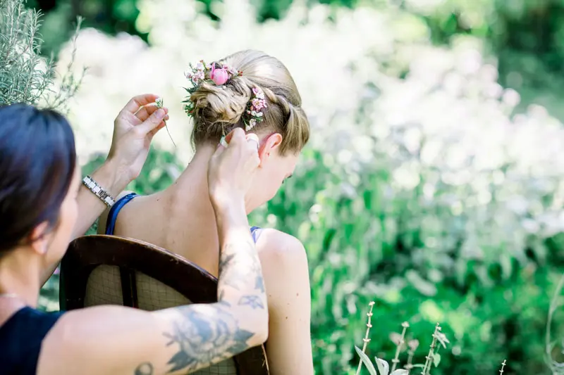 A friend pinning flowers into the bride's bun in the garden