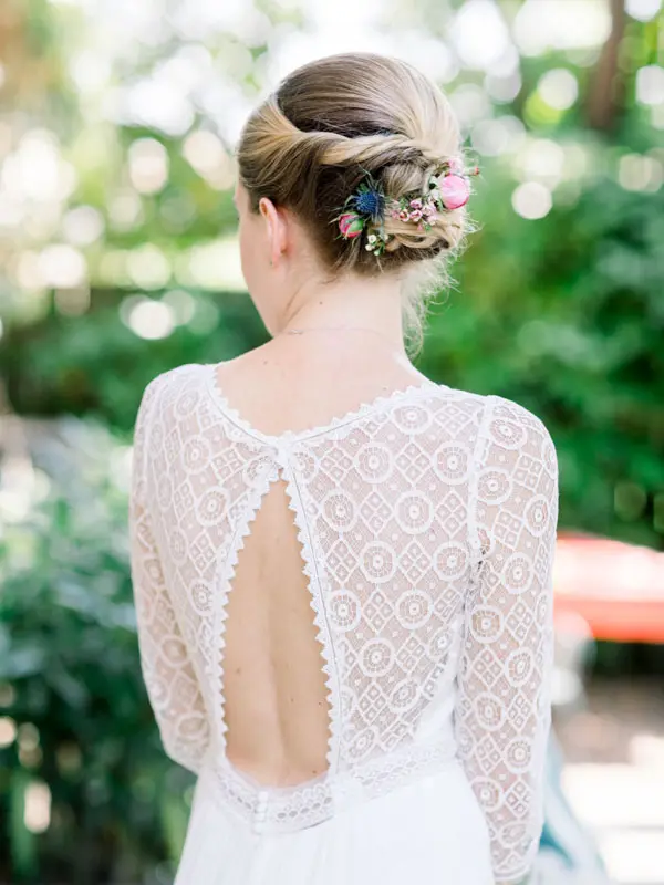 The open lace back of the bride's dress and her flower-adorned bun