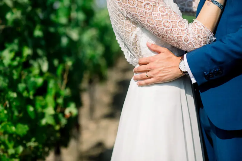 Detail of the couple embracing in the vines, lace dress and blue suit