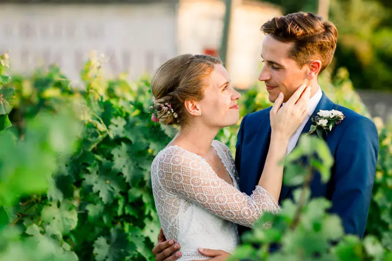 The bride touching the groom's face in the sunlit vines
