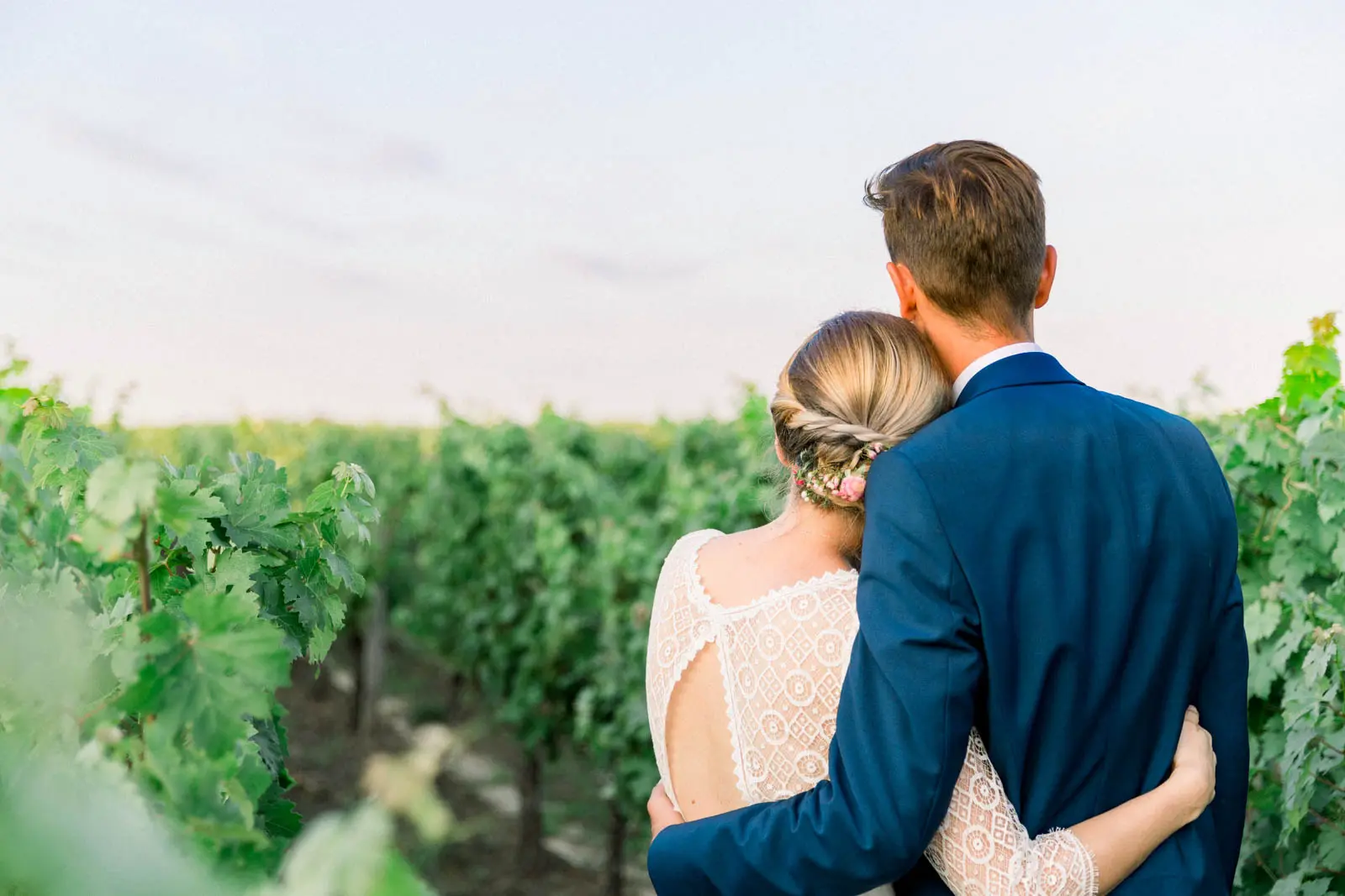 The newlyweds embracing with their backs to the camera, facing the vines at sunset