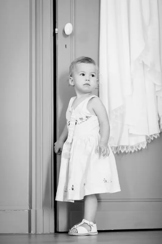 Little girl in a white dress standing in a doorway, in black and white