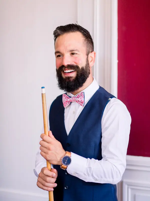 Bearded groom in a blue waistcoat and pink bow tie holding a billiard cue