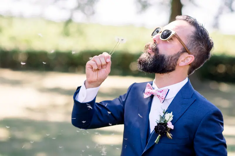 The groom in sunglasses blowing on a dandelion clock